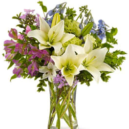 Bouquet of white lilies and purple flowers in a clear glass vase