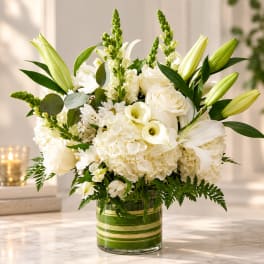 White floral arrangement with lilies, roses, and calla lilies in a glass vase