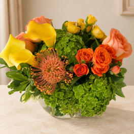 Bouquet of yellow calla lilies, orange roses, and green hydrangeas in a glass vase