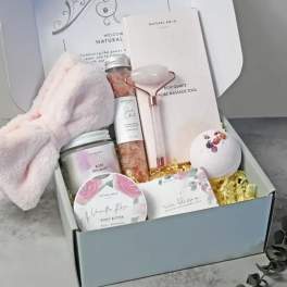 Spa gift box with pink headband, rose quartz roller, bath salts, candle, bath bomb, and body products