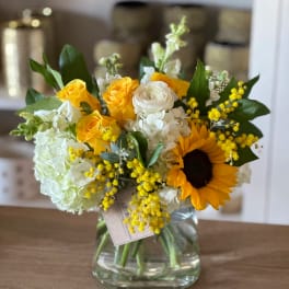 Bouquet of yellow roses, white blooms, and a sunflower in a glass vase