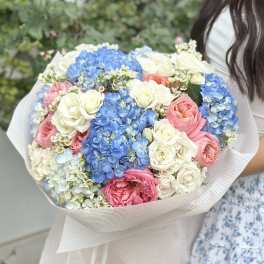Large bouquet of blue hydrangeas and pink and white roses wrapped in pale paper