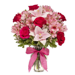 Bouquet of pink and red flowers in a glass vase with a pink ribbon