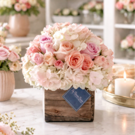 Pastel pink and white roses and hydrangeas arranged in a rustic wooden cube vase on a marble surface