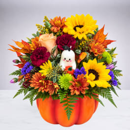 Fall flower arrangement in a pumpkin container with a small ghost decoration