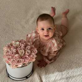 Baby beside a box of pale pink roses on a carpet