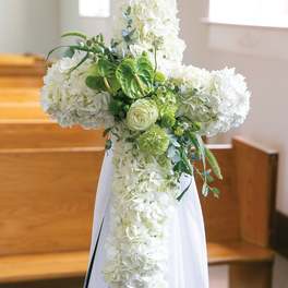White floral cross arrangement with green accents on a stand