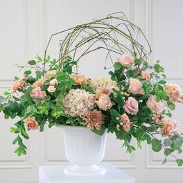 Pastel floral arrangement in a white pedestal vase with an arched twig frame