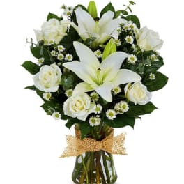 White lilies and roses in a glass vase with a burlap bow