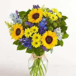 Bouquet of sunflowers, blue flowers, and yellow daisies in a glass vase