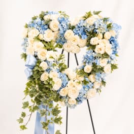 Heart-shaped floral wreath with cream roses and blue hydrangeas on a stand