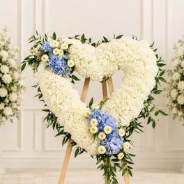 Heart-shaped white floral wreath with blue and yellow accents on a stand