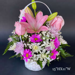 Pink lilies, roses, and daisies arranged in a white basket with a handle
