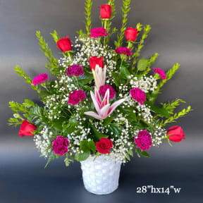 Tall bouquet of red roses, pink carnations, and white lilies in a white basket