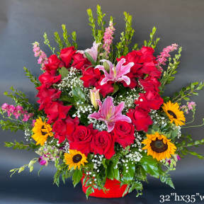 Large red rose and pink lily arrangement with sunflowers in a red container