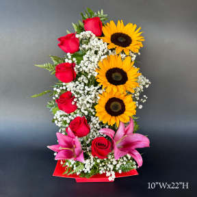 Tall arrangement of red roses, sunflowers, and pink lilies in a red container