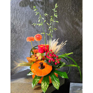 Orange floral arrangement in a pumpkin-shaped container with tall stems