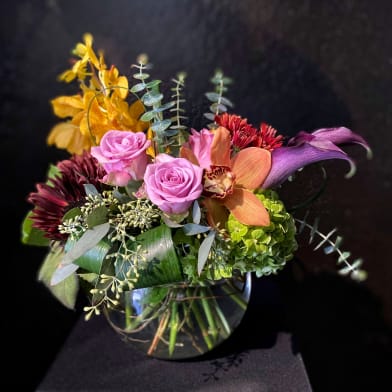 Mixed bouquet of pink roses, orange orchids, and green hydrangea in a glass vase
