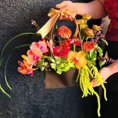 Handheld basket arrangement with orchids and bright mixed flowers
