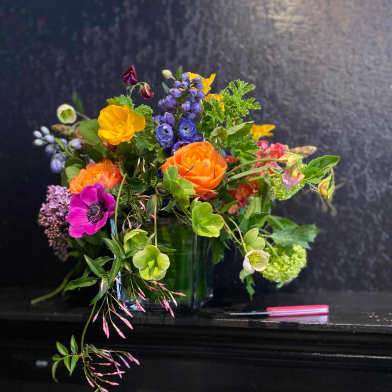 Colorful mixed bouquet in a glass vase with orange, yellow, purple, and pink blooms