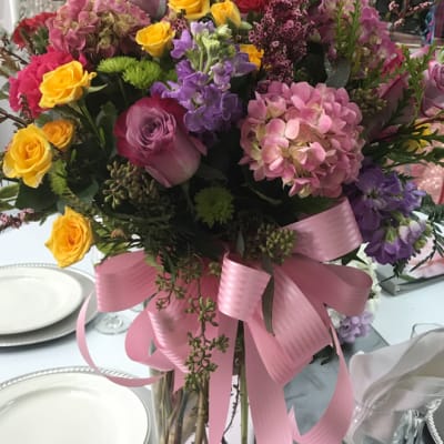 Mixed bouquet of pink, yellow, and purple flowers in a glass vase with a pink ribbon