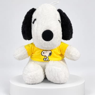 Snoopy plush toy wearing a yellow shirt on a white pedestal