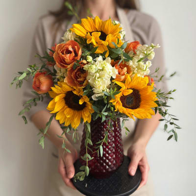 Bouquet of sunflowers, orange blooms, and white flowers in a red vase