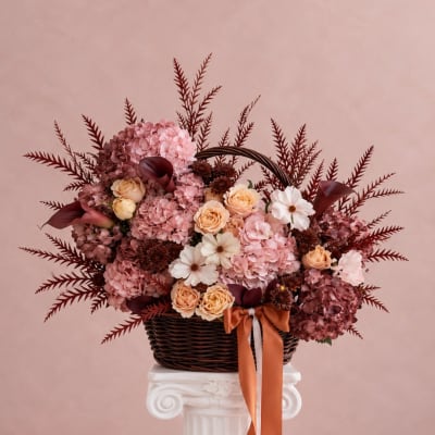 Pink and peach floral arrangement in a wicker basket with ribbon