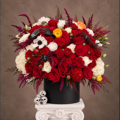 Red and white rose arrangement in a black vase with Halloween skull and spider accents