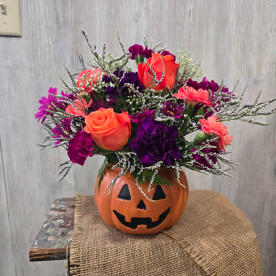 Orange and purple flower arrangement in a jack-o'-lantern vase