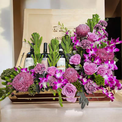 Pink and purple floral arrangement with wine bottles in a wooden box