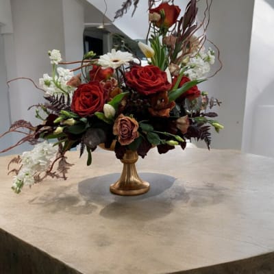 Red rose arrangement in a gold pedestal vase with white blooms
