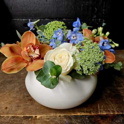Orange orchids and a white rose in a white bowl vase