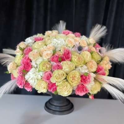 Round bouquet of pink, cream, and white roses in a black pedestal vase