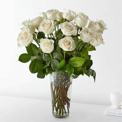 White roses arranged in a clear glass vase with green leaves