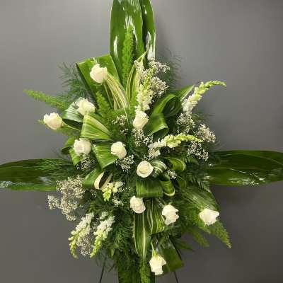 White roses and small white blooms arranged with glossy green leaves on a standing easel.