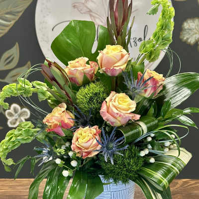 Mixed bouquet of peach roses and green foliage in a blue vase