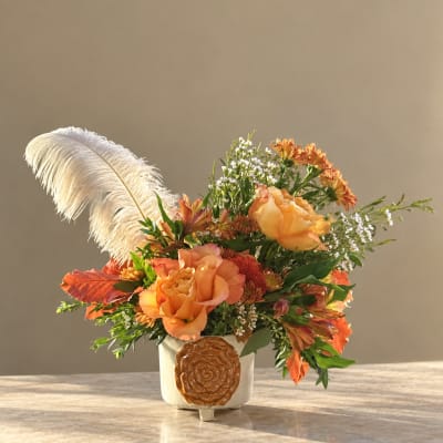 Orange floral arrangement in a white vase with a large white feather