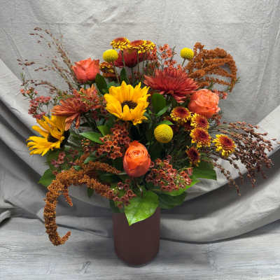 Autumn-toned arrangement with sunflowers, orange roses, and mums in a matte brown cylinder vase