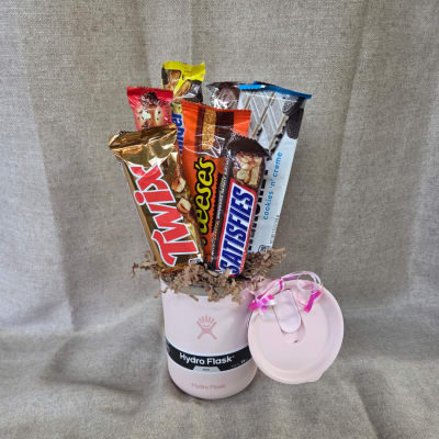 Pink Hydro Flask mug filled with assorted candy bars and a ribboned lid beside it