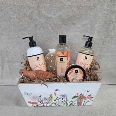 Bath gift set with orange ginger products in a floral-printed white wooden box filled with paper shred.