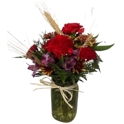 Red and purple mixed bouquet in a glass vase with a raffia bow