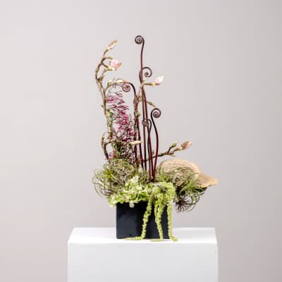 Tall floral arrangement with pink blossoms and curly branches in a black container
