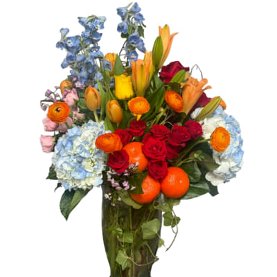Mixed bouquet with roses, hydrangeas, lilies, and oranges in a tall vase