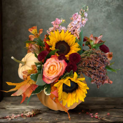 Fall floral arrangement in a pumpkin container with sunflowers and roses