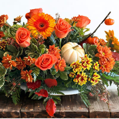 Autumn floral arrangement with orange roses, gerbera daisies, and small pumpkins