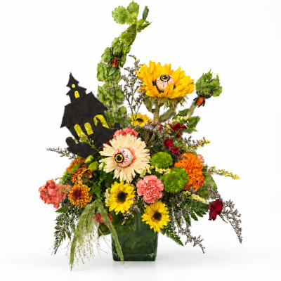 Halloween floral arrangement with sunflowers, carnations, and a haunted house decoration in a vase
