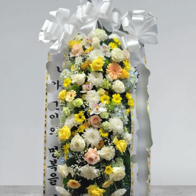 Tall standing floral spray with white ribbon and mixed yellow, white, and peach flowers