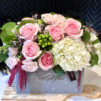Pink roses and white hydrangeas arranged in a gray gift box