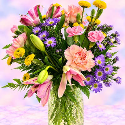 Mixed bouquet of pink lilies, carnations, and purple daisies in a glass vase